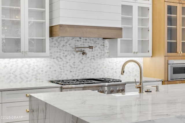 kitchen featuring light stone countertops, glass insert cabinets, white cabinets, and backsplash