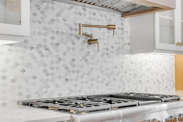 room details featuring white cabinetry, tasteful backsplash, glass insert cabinets, and stove