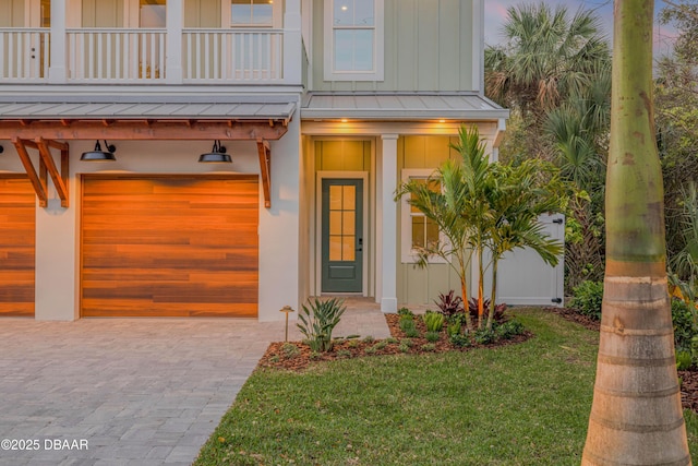 entrance to property featuring a lawn, a balcony, an attached garage, a standing seam roof, and board and batten siding