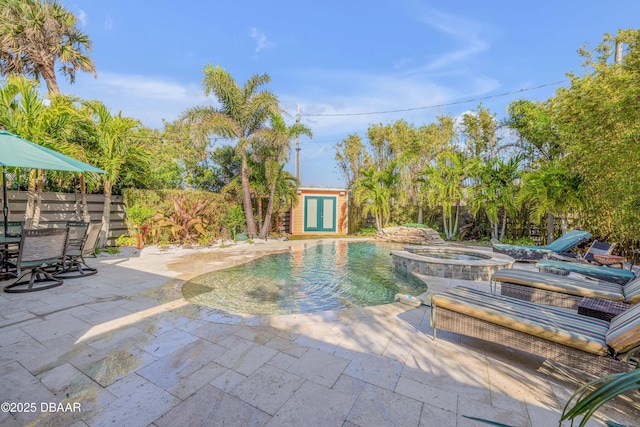 view of pool with an outbuilding, a patio area, fence, and a pool with connected hot tub