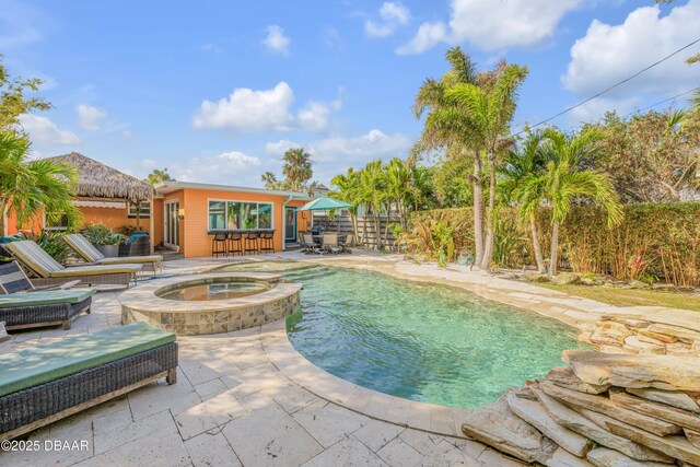 view of pool featuring a patio area, a pool with connected hot tub, fence, and an outdoor bar