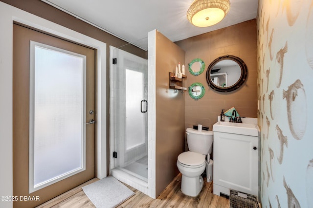 bathroom with toilet, a stall shower, a sink, and wood finished floors