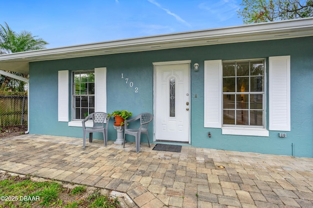 doorway to property with covered porch, fence, and stucco siding