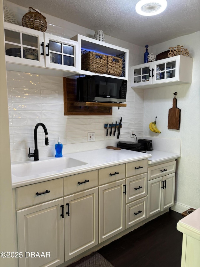 bar featuring a textured ceiling, dark wood-type flooring, backsplash, and a sink