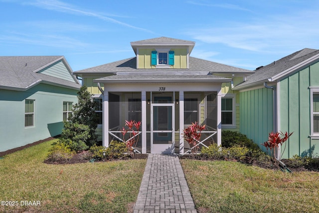 view of front facade with a sunroom, a shingled roof, board and batten siding, and a front yard