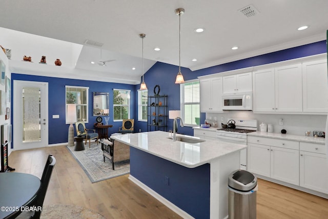 kitchen with white appliances, an island with sink, light wood-style flooring, white cabinetry, and a sink