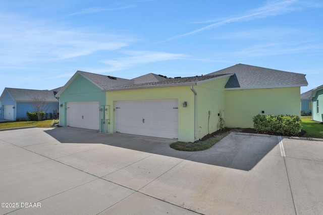 view of side of property featuring concrete driveway, roof with shingles, an attached garage, and stucco siding