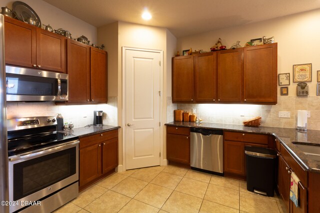 kitchen featuring dark stone countertops, tasteful backsplash, light tile patterned flooring, and stainless steel appliances