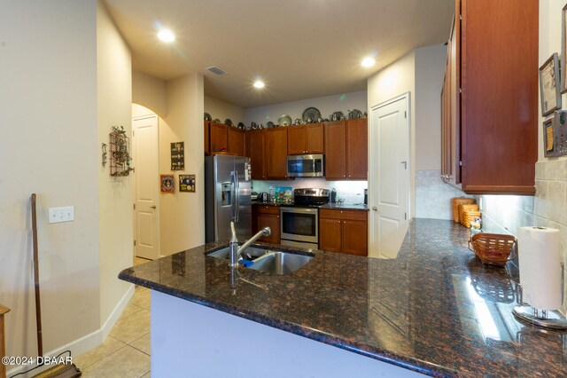 kitchen with sink, kitchen peninsula, appliances with stainless steel finishes, dark stone counters, and light tile patterned floors