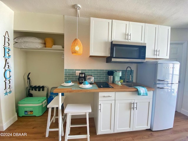kitchen with stainless steel microwave, a sink, backsplash, white cabinets, and freestanding refrigerator
