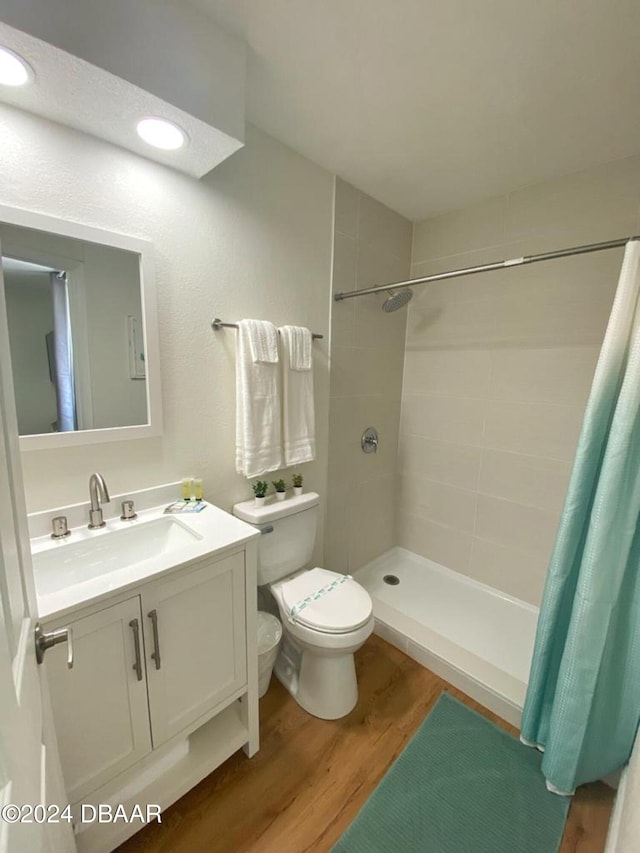 bathroom with wood finished floors, tiled shower, toilet, and vanity