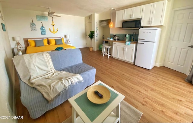 bedroom with light wood-type flooring, freestanding refrigerator, and baseboards