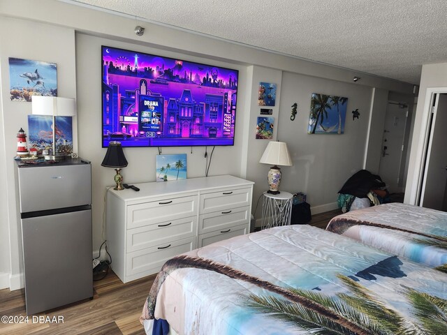 bedroom featuring wood-type flooring, a textured ceiling, and stainless steel refrigerator