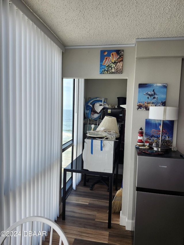 bedroom with dark hardwood / wood-style flooring, a water view, a textured ceiling, and stainless steel refrigerator