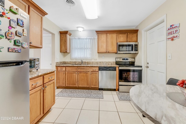 kitchen featuring appliances with stainless steel finishes, light tile patterned floors, sink, and light stone countertops