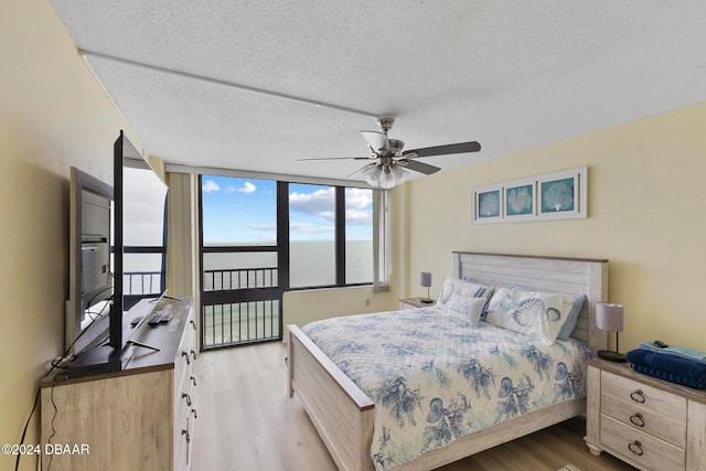 bedroom featuring ceiling fan, expansive windows, light hardwood / wood-style floors, and a textured ceiling