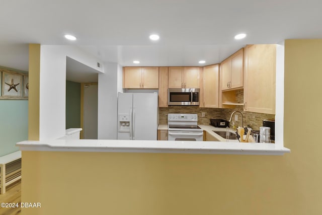 kitchen with tasteful backsplash, kitchen peninsula, light brown cabinets, and white appliances