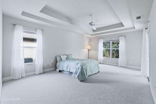 bedroom featuring light carpet, a raised ceiling, and ceiling fan