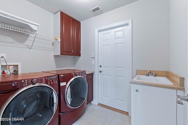 washroom featuring cabinets, sink, a textured ceiling, light tile patterned flooring, and washing machine and clothes dryer