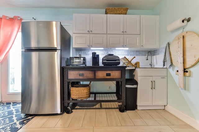 kitchen with tasteful backsplash, white cabinetry, sink, and stainless steel refrigerator