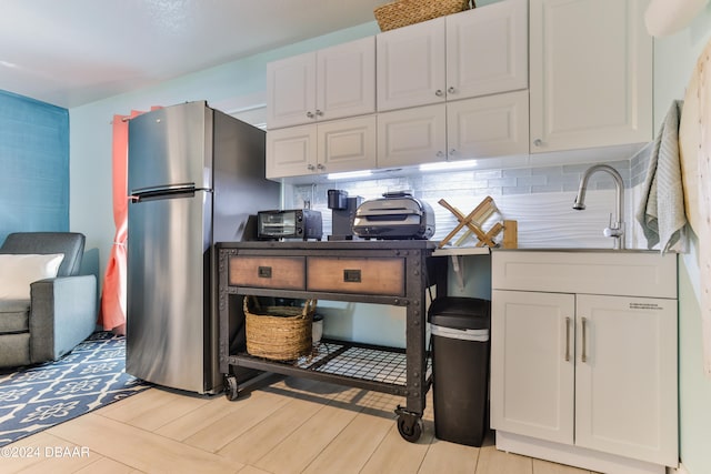 kitchen featuring light tile patterned flooring, stainless steel fridge, sink, decorative backsplash, and white cabinets