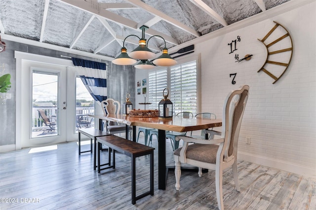 dining room featuring hardwood / wood-style flooring, brick wall, french doors, a notable chandelier, and vaulted ceiling