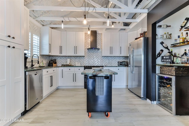 kitchen featuring white cabinetry, appliances with stainless steel finishes, beam ceiling, light hardwood / wood-style flooring, and wall chimney range hood