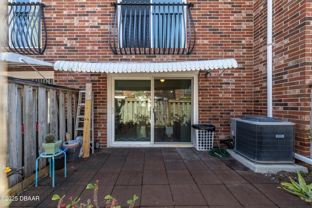 doorway to property with a patio, fence, central AC unit, and brick siding