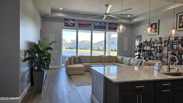 kitchen featuring sink, decorative light fixtures, a center island with sink, a tray ceiling, and light stone countertops