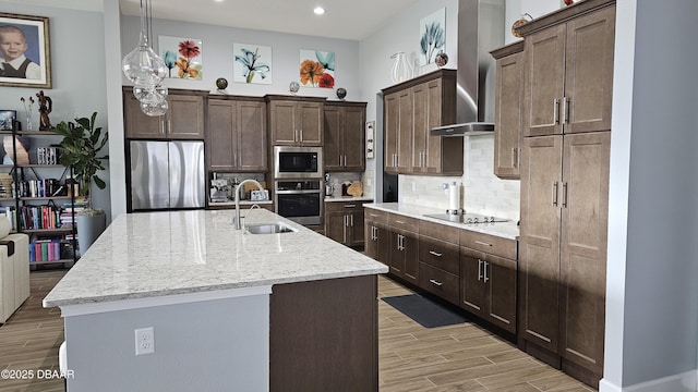 kitchen featuring wall chimney exhaust hood, sink, a center island with sink, stainless steel appliances, and backsplash