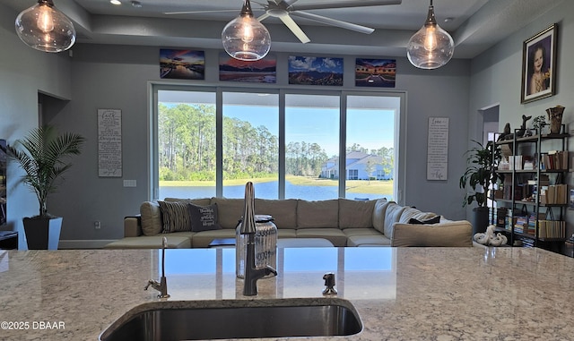 kitchen featuring a water view, light stone countertops, sink, and hanging light fixtures