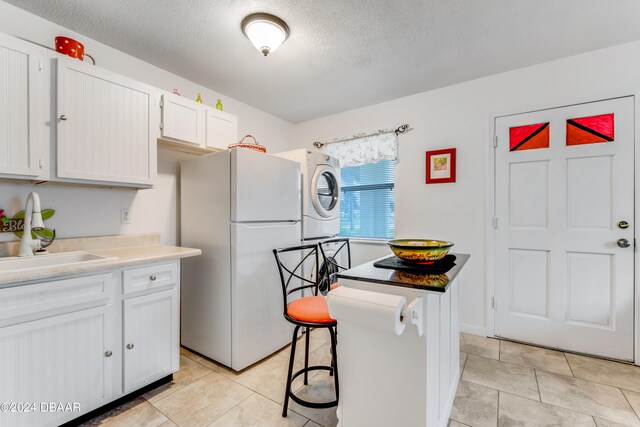 kitchen with white cabinetry, sink, a kitchen bar, stacked washer and dryer, and white refrigerator