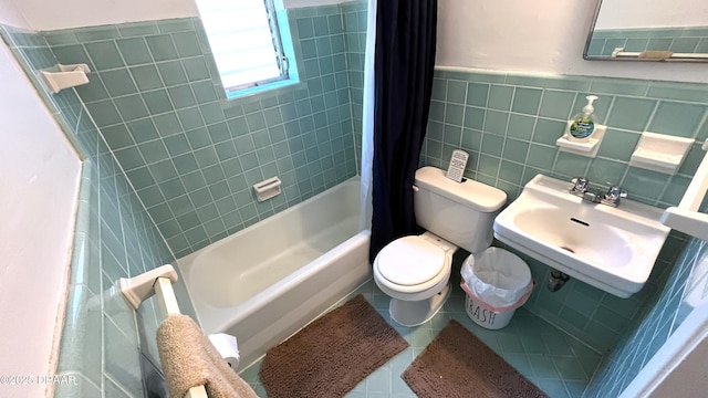 full bath with tile patterned floors, shower / bathtub combination with curtain, toilet, a sink, and tile walls