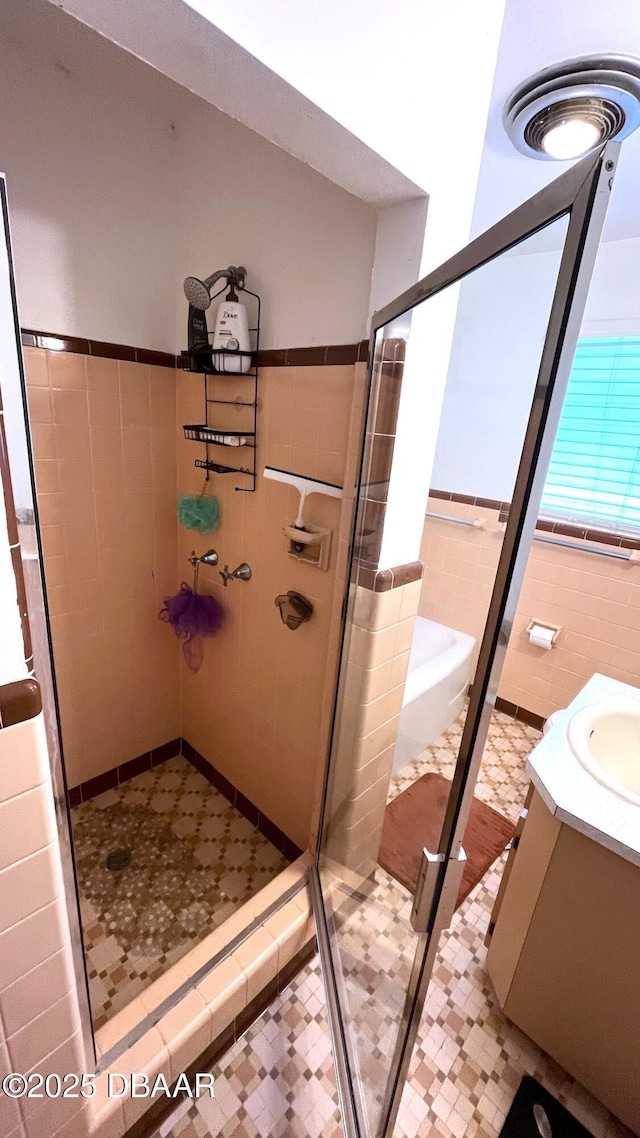 full bathroom with tile patterned floors, a wainscoted wall, a stall shower, tile walls, and vanity