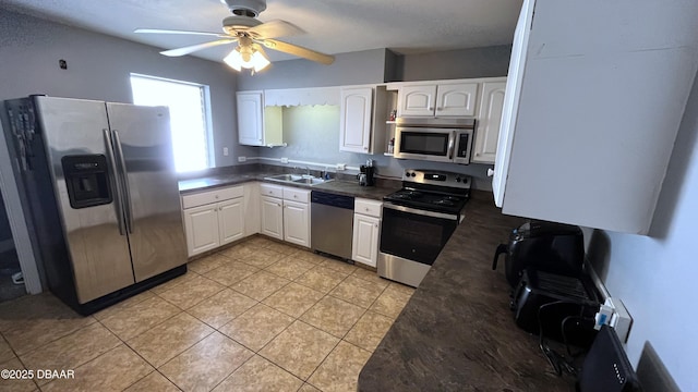 kitchen with dark countertops, light tile patterned floors, stainless steel appliances, white cabinetry, and a sink