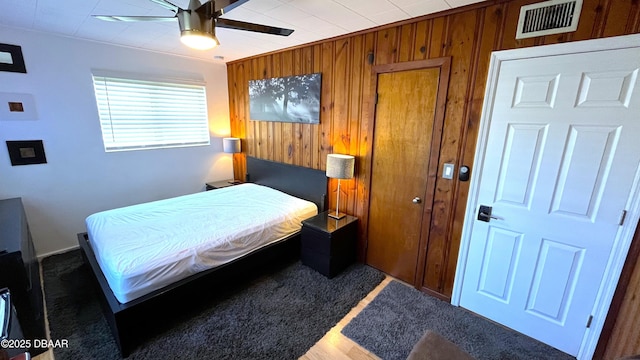 bedroom featuring visible vents, wooden walls, ceiling fan, and ornamental molding