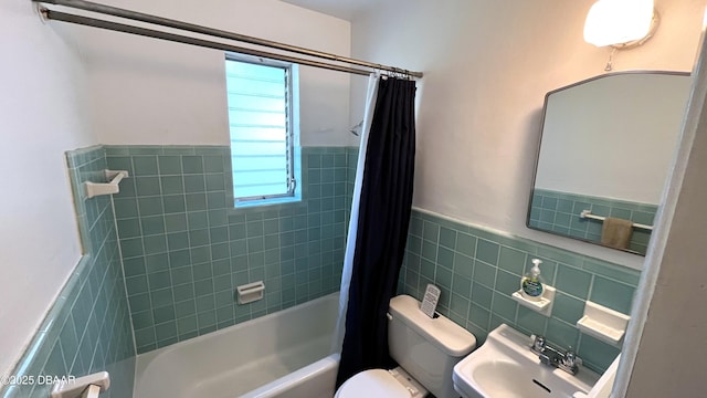 full bath featuring shower / bathtub combination with curtain, a wainscoted wall, a sink, tile walls, and toilet