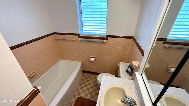 bathroom featuring a tub, toilet, wainscoting, tile patterned floors, and a sink