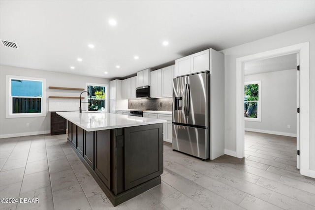 kitchen featuring white cabinets, appliances with stainless steel finishes, an island with sink, and plenty of natural light