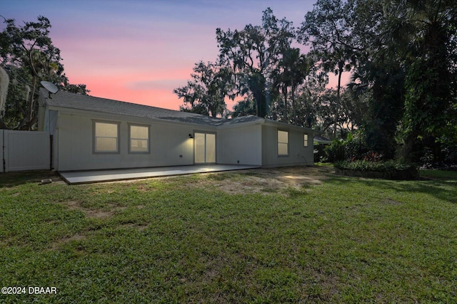 back house at dusk featuring a patio area and a yard