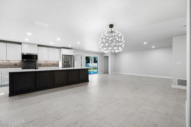 kitchen with appliances with stainless steel finishes, backsplash, an island with sink, a chandelier, and white cabinets