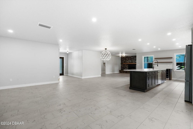 kitchen with stainless steel appliances, dark brown cabinets, a large fireplace, and a kitchen island with sink