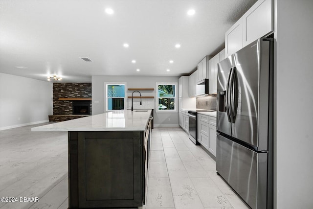 kitchen with appliances with stainless steel finishes, light stone countertops, sink, white cabinets, and a kitchen island with sink