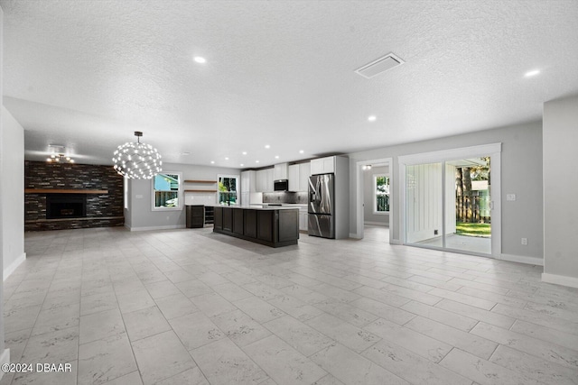 unfurnished living room featuring a textured ceiling, a notable chandelier, and a brick fireplace