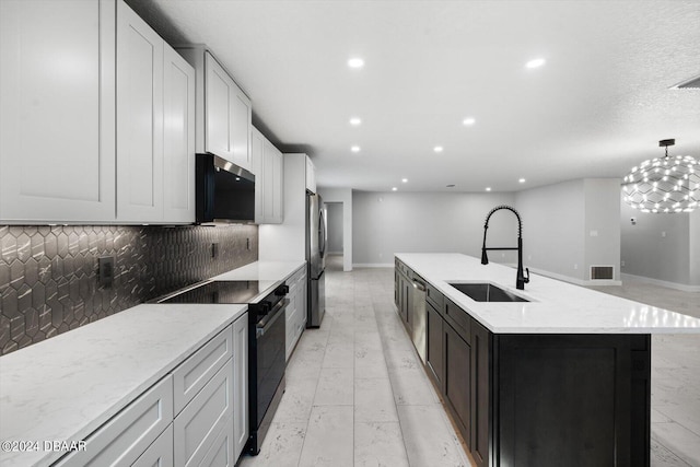 kitchen featuring a center island with sink, backsplash, appliances with stainless steel finishes, hanging light fixtures, and sink