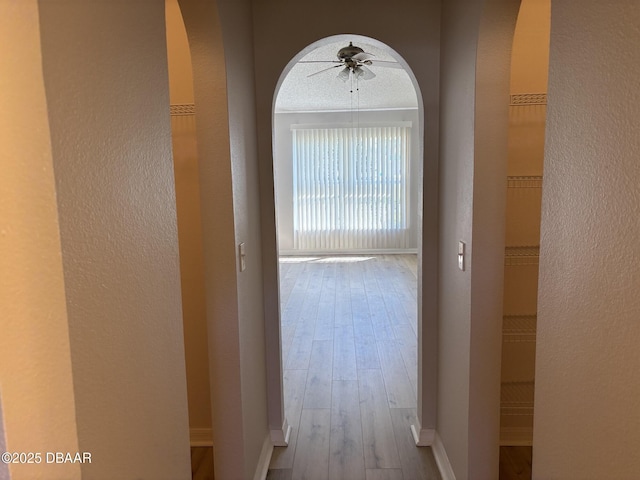 hallway featuring light wood finished floors, baseboards, arched walkways, and a textured wall