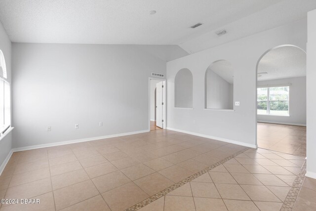 tiled spare room with vaulted ceiling and a textured ceiling