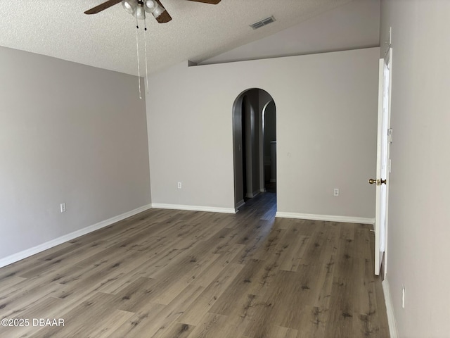 empty room featuring arched walkways, dark wood-style flooring, visible vents, vaulted ceiling, and a textured ceiling