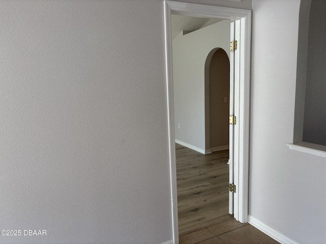 hall with baseboards, arched walkways, and dark tile patterned flooring