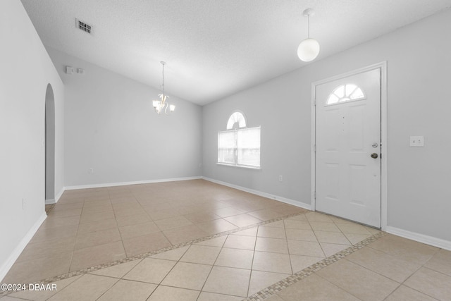 foyer with a textured ceiling, light tile patterned floors, lofted ceiling, and a notable chandelier